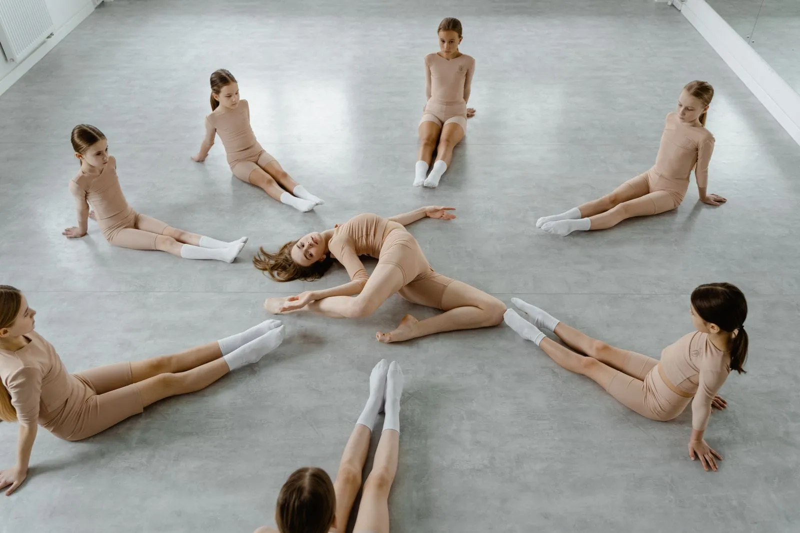 A group of young female dancers in a dance studio practicing flexibility and coordination.