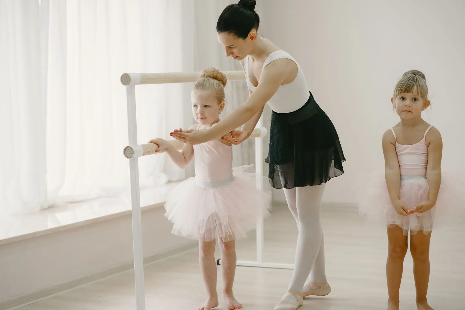 Ballet teacher assisting young dancers in a class, enhancing their skills and confidence.